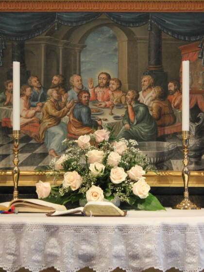 Altaret i Esse kyrka. Den nedre altartavlan, föreställande nattvarden, syns på bilden. fyra ljus, blommor och en öppen bibel.