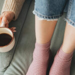 En person sitter på en soffa med en kaffekopp bredvid sig. Man ser bara fötterna på personen.