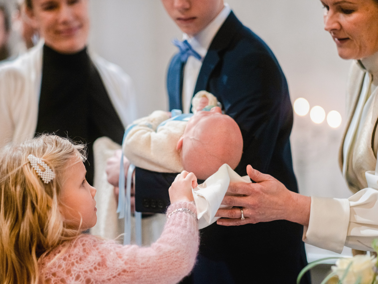 En liten flicka hjälper prästen att torka det döpta barnets huvud.