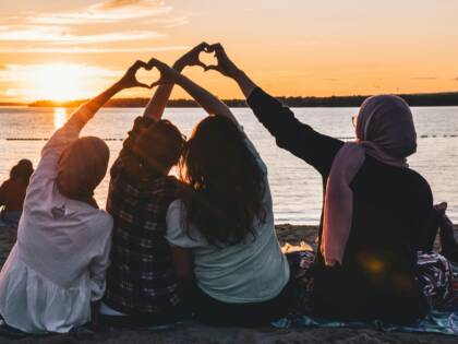 Ungdomar på en strand, bildar hjärtan av sina händer.